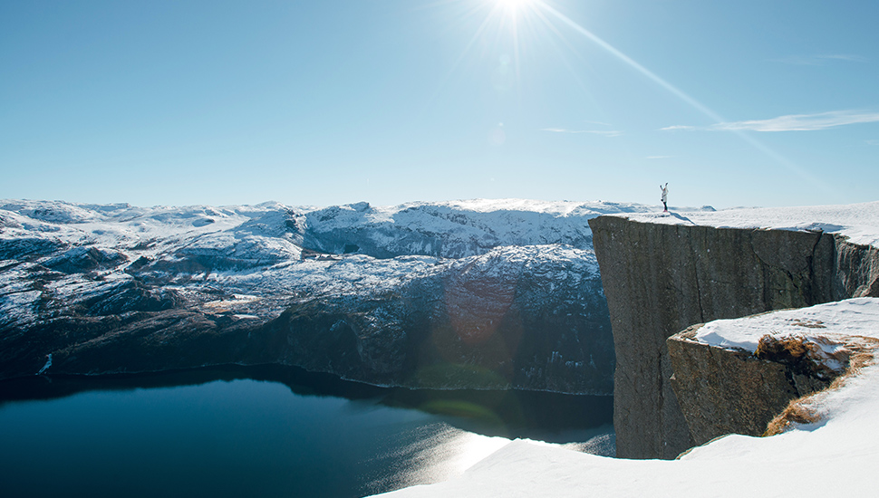 woman standing on Norwegian cliff edge with raised hands