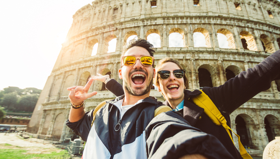 Happy couple taking a selfie in front of the colosseum in Rome