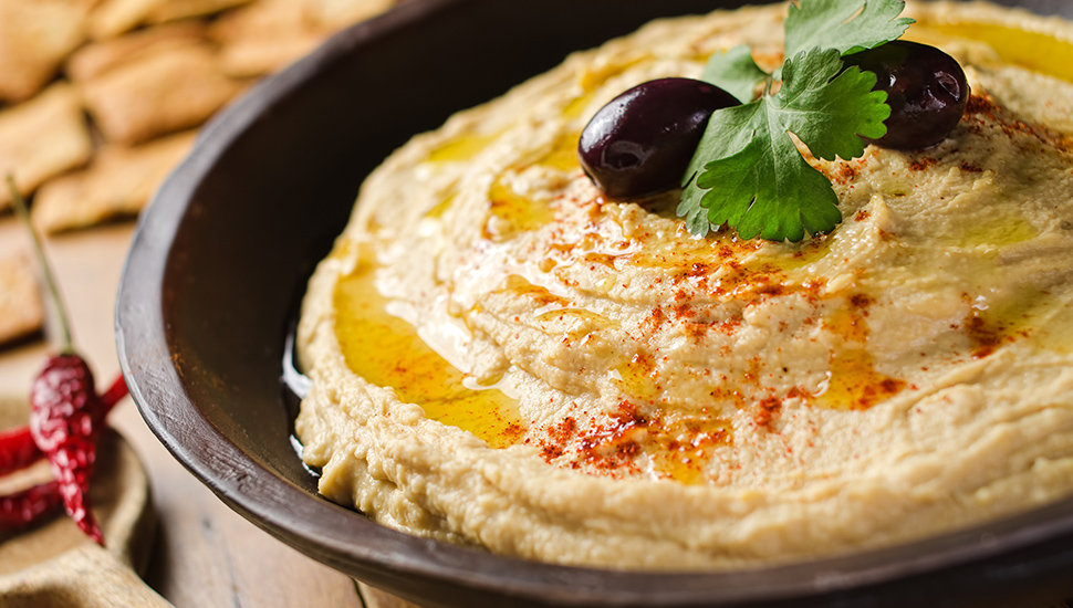 A bowl of creamy hummus with olive oil and pita chips.
